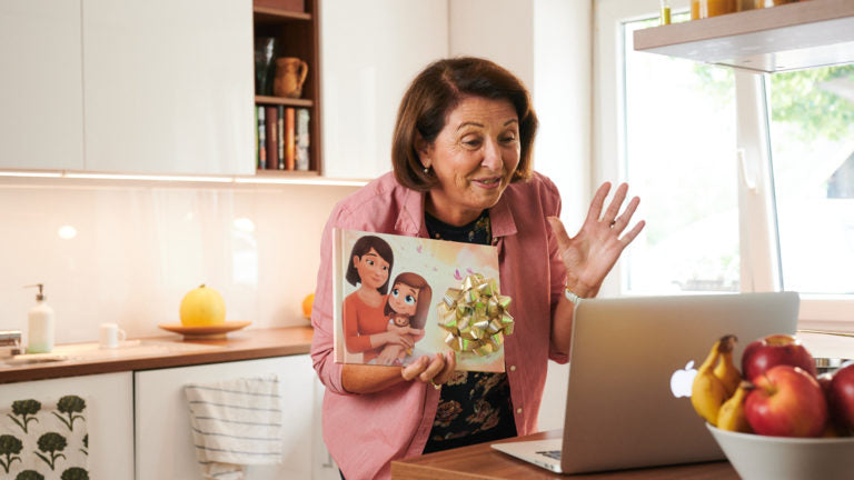 Una nonna mostra il suo libro personalizzato tramite lo zoom del computer portatile mentre si trova in cucina.
