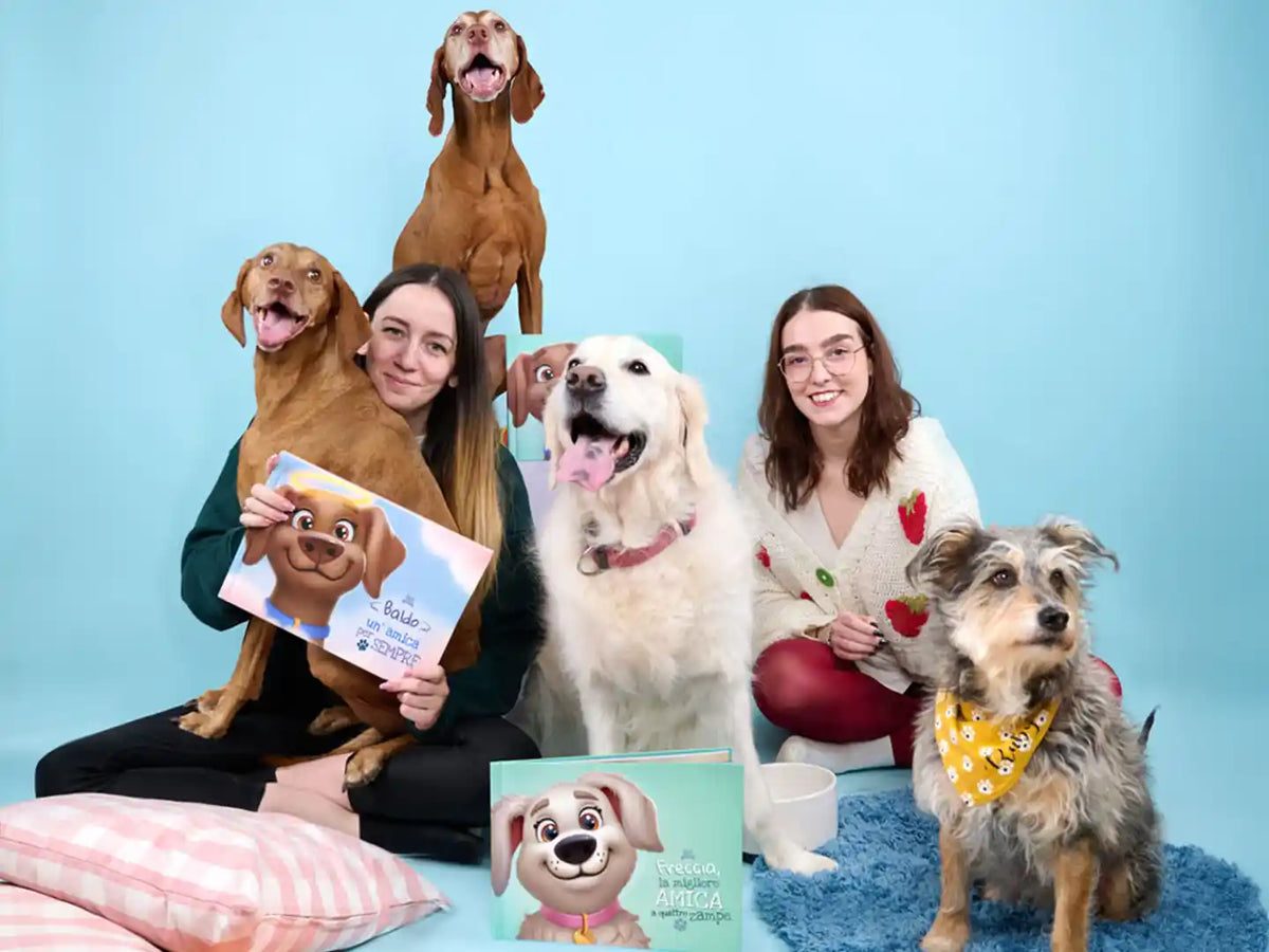 Proprietari con i loro cani che tengono libri personalizzati di Urrá Eroi s con titoli come "Baldo un' amico per sempre" e "Freccia, la migliore a quattro zampe"—perfetti per celebrare la vita dopo il ponte dell’arcobaleno.