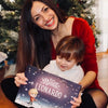 Una madre seduta con il suo bambino davanti all'albero di Natale che sorride e mostra il regalo più carino di Urrà Eroi. 