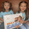 Due sorelle con in mano un libro personalizzato sullo stare a casa da sole.